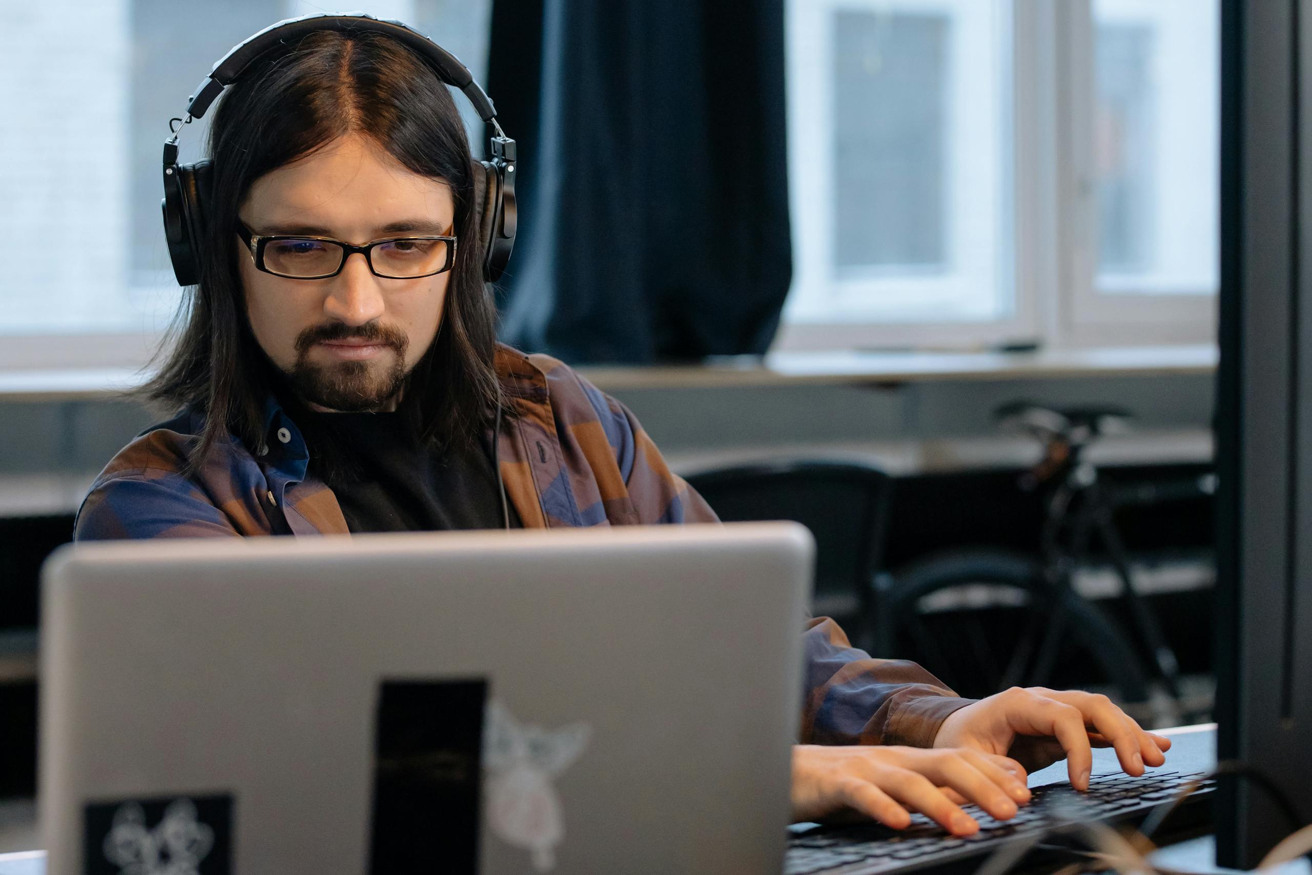Office worker wearing headphones while concentrating on laptop tasks.